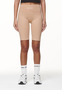 Beiga cykelshorts med hög midja, tillverkade av elastiskt tyg. Har en vit logotyp vid midjan och en slät, strömlinjeformad design.