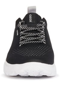 Zapatilla negra con parte superior de malla transpirable, suela de goma blanca, cuello acolchado y cordones con un patrón en blanco y negro. Presenta un logo en el costado.