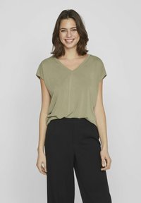 Olivgrön V-ringad topp med korta ärmar, lös passform och mjuk textur, i kombination med skräddarsydda svarta byxor. Minimalistisk design.