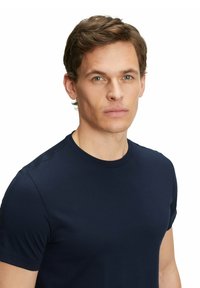 Granatowa koszulka z krótkim rękawem wykonana z miękkiego, gładkiego materiału. Ma okrągły dekolt i dopasowany krój. Minimalistyczna, bez widocznych logo.