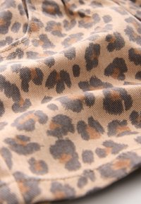 Tissu beige avec un gros plan d'un motif léopard dans des tons gris foncé et marron, montrant la texture et les détails des coutures.
