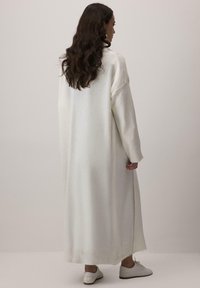 Dlhý, nadmerný biely pletený sveter s rebrovanými manžetami a spodným lemom. Hladká textúra, minimalistický dizajn a postranné rozparky pre väčšie pohodlie pri pohybe.