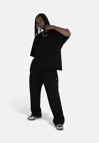 Black oversized t-shirt paired with black pants, featuring a relaxed fit. Shoes are silver with a sleek design. Simple, monochrome outfit.