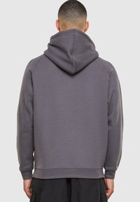 Sudadera de color gris carbón con una gran capucha ajustable, mangas raglán y puños acanalados; confeccionada en una suave tela texturizada y con un corte relajado.