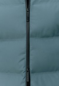 Vadderad ytterkläder i dämpad teal-färgad tyg med en slät textur, med en central svart dragkedja och en minimalistisk design.