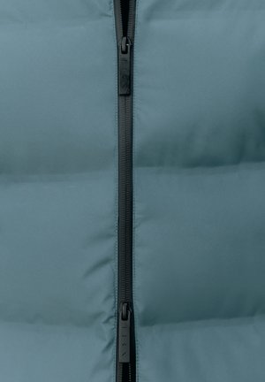 Vycpaná svrchní bunda v tlumené tyrkysové látce s hladkou texturou, s centrálním černým zipem a minimalistickým designem.