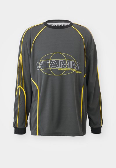 Γκρι πουκάμισο με μακριά μανίκια και κίτρινες λεπτομέρειες, που διαθέτει ένα σχέδιο λογότυπου στο κέντρο. Κατασκευασμένο από ένα λείο, ελαφρύ ύφασμα.