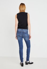 Tettsvarende svart ermeløs topp og mørkeblå smale jeans. Glatt stoff, standard fem-lommers design med synlige sømmer og baklommer.