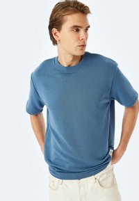 Blå bomullst-shirt med kort ärm och rund halsringning. Har en liten logotyp på sidan och en mjuk yta.