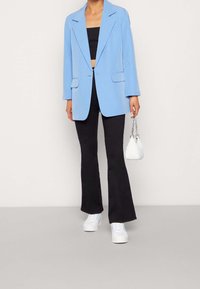 Lichtblauwe op maat gemaakte blazer met gesneden revers, twee voorzakken, gecombineerd met een zwarte crop top, uitlopende zwarte broek en witte sneakers.