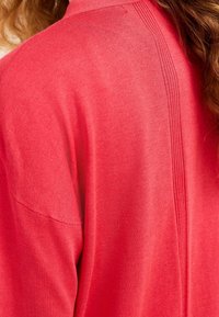 Suéter de punto rojo con un ajuste relajado, detalles acanalados en la parte trasera y textura suave. Cuenta con mangas cortas y un escote redondo.