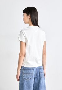 Witte katoenen t-shirt met korte mouwen, een ronde halslijn en een klein driehoekig ontwerp op de achterkant, gecombineerd met blauwe denim shorts.