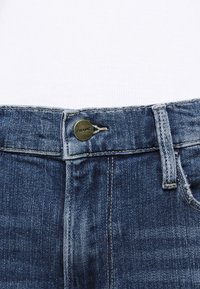 Jeans de mezclilla azul oscuro con corte recto, que cuentan con un botón de latón con el logo "FRAME" y paradas de cinturón estándar. Tejido texturizado con un ligero desgaste.
