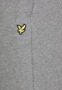 Grått tyg med en liten broderad gul fågel-emblem som är omramad i svart nära en vertikal söm.