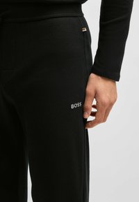 Svart termiske joggebukser med teksturert stoff, prydet med en brodert "BOSS"-logo på låret og en subtil aksent nær midjen.