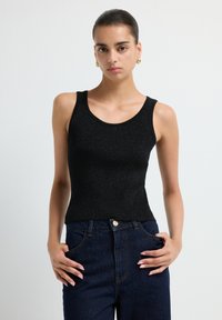 Top de tirantes negro acanalado con un diseño ajustado y tirantes anchos, combinado con jeans de mezclilla oscuros. La tela tiene un brillo sutil y una textura.