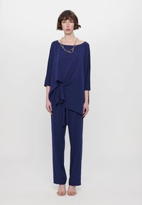 Námořnický modrý dvoudílný outfit se volným topem s točeným detailem a rovnými kalhotami, vyrobený z hladké tkaniny.