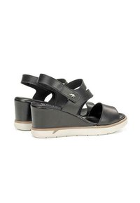 Sandalias de cuña negras con punta abierta, que presentan doble tira y una suela acolchada. El tacón mide aproximadamente 7 cm, con un acabado en cuero suave.