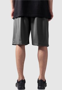 Sorte atletiske shorts laget av pustende stoff, kne-lange med en glatt tekstur og sidelommer, sammen med sorte joggesko.