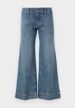 Jeans de denim anchos y azul con presillas para cinturón, cierre de botón y detalles de costura visibles sobre un fondo blanco.