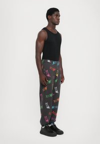 Grijze joggings met kleurrijke, gestileerde konijnenprints, taps toelopend bij de enkels. Gedragen met een zwart mouwloos topje en zwarte sneakers.