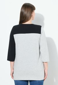 Top a maniche lunghe grigio e nero con design a color block, dotato di collo rotondo e texture morbida. Vista posteriore mostrata, che evidenzia il contrasto.