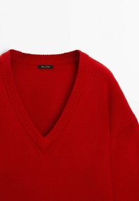 Pull en tricot rouge avec un design en V, col côtelé et texture douce. Présente une coupe ample et ne comporte ni motifs visibles ni accessoires.