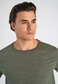 Oliwkowa koszulka z okrągłym dekoltem z teksturowanej tkaniny, charakteryzująca się dopasowanym krojem i gładkim, miękkim wykończeniem.