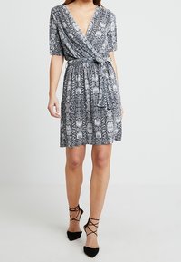 Vestido envolvente en estampado de serpiente en blanco y negro, con escote en V, mangas cortas, cintura ceñida con cinturón y falda fluida. Tejido suave y texturizado.