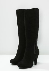 Bottes noires en daim montantes avec un design élégant, un bout effilé et un talon bloc. Présente un panneau d'accent brillant sur le côté.
