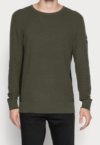 Maglione lavorato a maglia verde con maniche lunghe, scollatura rotonda e pannelli laterali neri. Presenta polsini e orlo a costine, con dettaglio del logo sulla manica.
