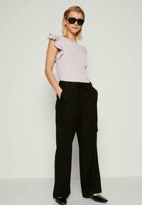 Lilac top with ruffled sleeves, paired with black wide-leg cargo pants. Model wears black sunglasses and black slip-on shoes.