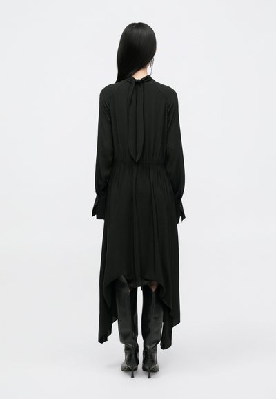 Čierne šaty s vysokým a nízkym lemom, dlhými rukávmi a viazaním okolo krku. Vyrobené z ľahkej látky, skombinované s čiernymi čižmami po kolená.