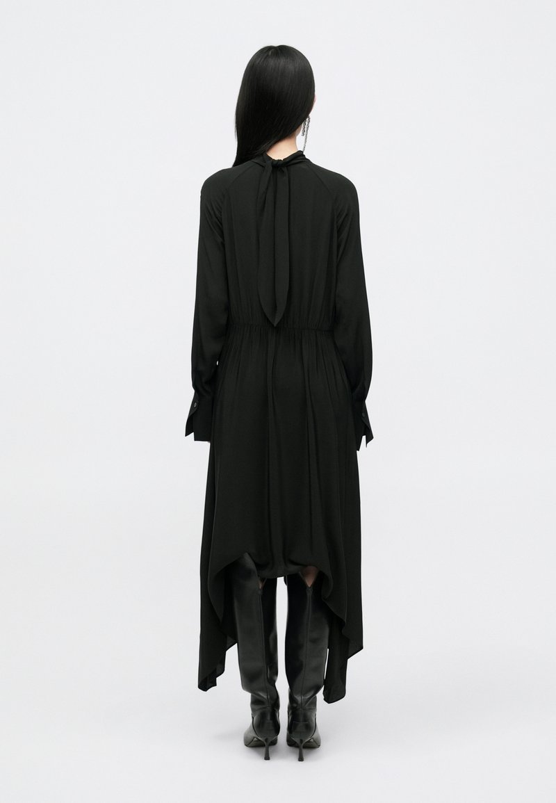 Vestido negro con un dobladillo asimétrico, mangas largas y un lazo en el cuello. Hecho de una tela ligera, combinado con botas negras hasta la rodilla.