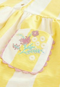Tessuto a righe giallo e bianco con una toppa quadrata ricamata con fiori rosa, bianchi e blu, bordata con un bordo all'uncinetto rosa.