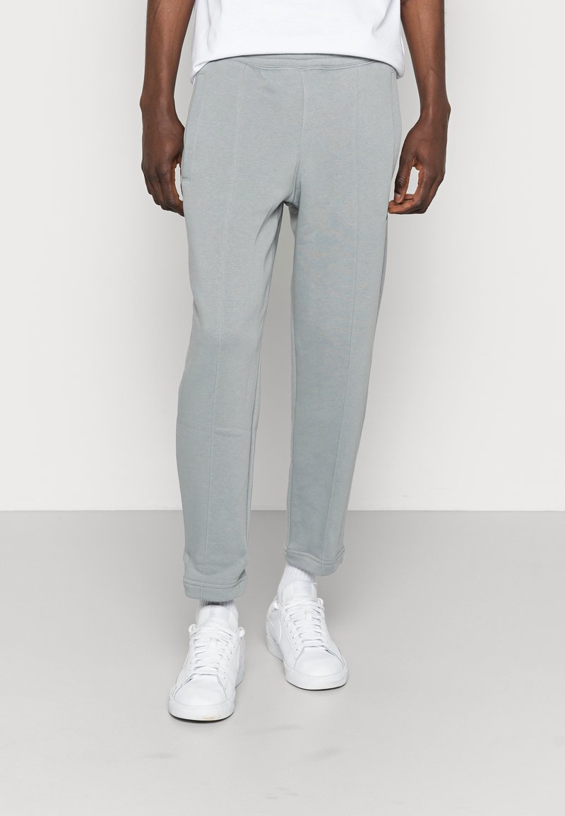 Light gray sweatpants with a tapered design, made from soft material, featuring side pockets and elastic cuffs, paired with white sneakers.