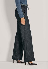 Wijd uitlopende broek in donker gestreepte stof met een elastische tailleband. Gecombineerd met puntige, glanzende zwarte hakken.