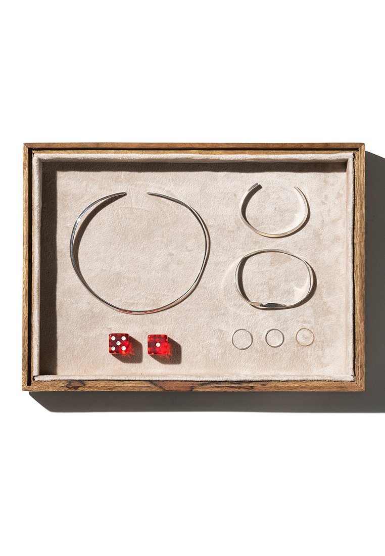 Schmuckset in einer Holzkiste mit beigem Stoffbezug. Enthält silberne Ohrstecker, Ringe und rote Würfel mit weißen Punkten.