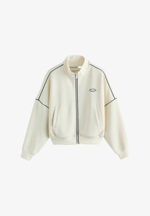 Veste zippée crème avec des détails noirs, deux poches avant, un col montant et un petit logo sur la poitrine. Tissu doux et coupe décontractée.