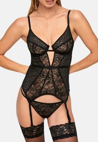 Schwarzer Spitzensbody mit strukturierten Cups, Cut-out-Details, verstellbaren Trägern und angebrachten Strümpfen; kombiniert mit einem passenden Tanga darunter.