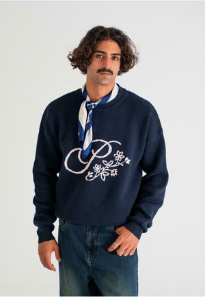 Marineblå sweater med lyserød blomsterbroderi og bogstavet "P" fortil. Rund halsudskæring og ribkantede manchetter. Kombineret med denim jeans.