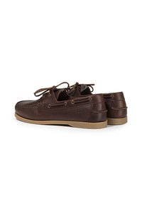 Chaussures de bateau en cuir marron avec un bout rond, un laçage, une semelle en caoutchouc contrastante couleur tan, et un détail de logo embossé sur le côté.