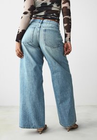 Breda ben jeans i blå denim med en urtvättad finish, två bakfickor och råkant. Tillsammans med en mönstrad långärmad topp.