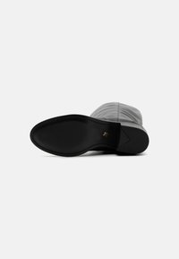 Gray ankle boot with a smooth, textured upper, black outsole, and subtle gold accent on the heel. Curved shape with no visible laces.