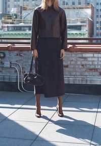 Czarna skórzana kurtka typu cropped z dwoma przednimi kieszeniami, połączona z ciemną midową spódnicą. Dodatki to mała torebka i szpilki.