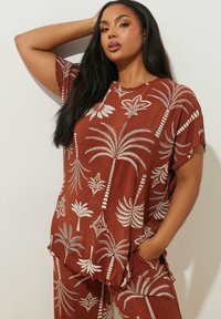Set di camicia e pantaloni a righe marroni con motivi di palme e foglie bianchi. Vestibilità ampia con bordi ondulati, maniche corte e tasche.