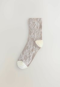 Beige zokni fehér virágos csipkepatternnel, szilárd fehér lábujj- és sarokrészekkel, sík helyzetben, világos háttér előtt.