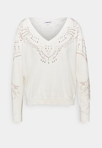 Crème kleurige trui met een V-hals, voorzien van decoratieve gouden studs met bloempatronen langs de halslijn en mouwen. Geribbelde manchetten en zoom.