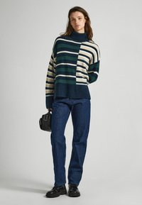 Maglione a collo alto a righe in blu navy, verde e crema, abbinato a pantaloni in corduroy blu navy. Presenta una vestibilità rilassata e polsini a costine.