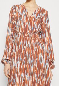 Vestido de manga larga con escote en V, cintura ajustada y estampado ikat multicolor en tonos óxido, crema y azul. Textura de tela suave.
